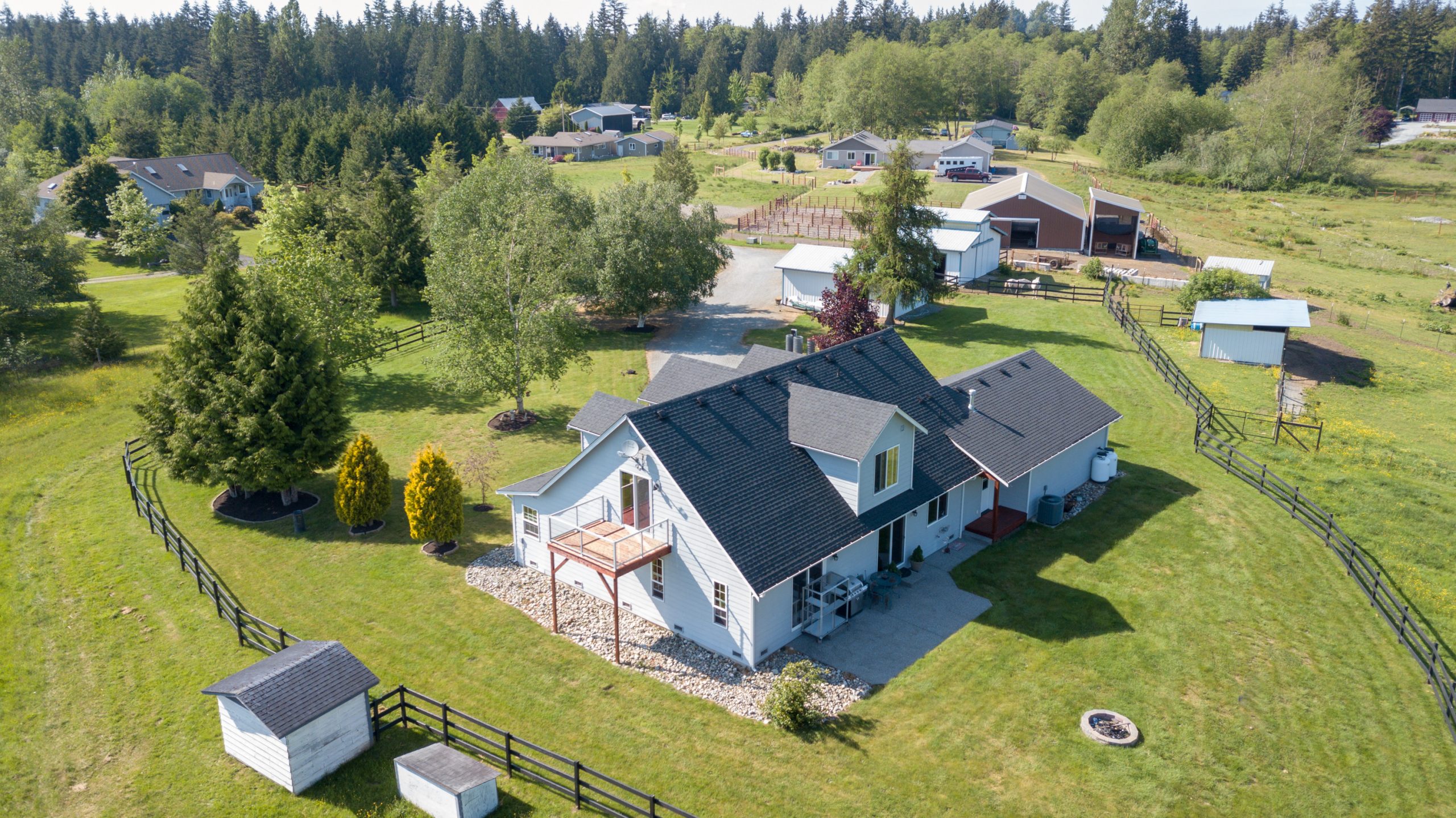 Drone photo of single farm house with grey roof and large green grass yard.